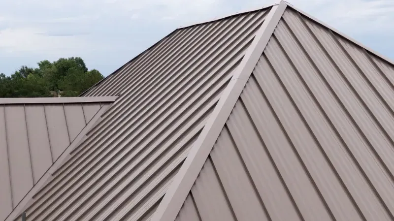 A close up of a brown metal roof with trees in the background