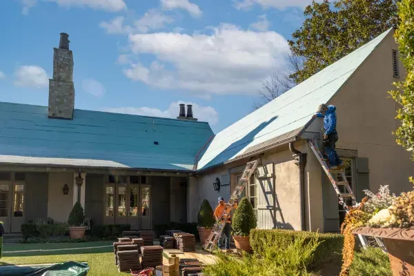 A man is painting the roof of a house with a blue roof.