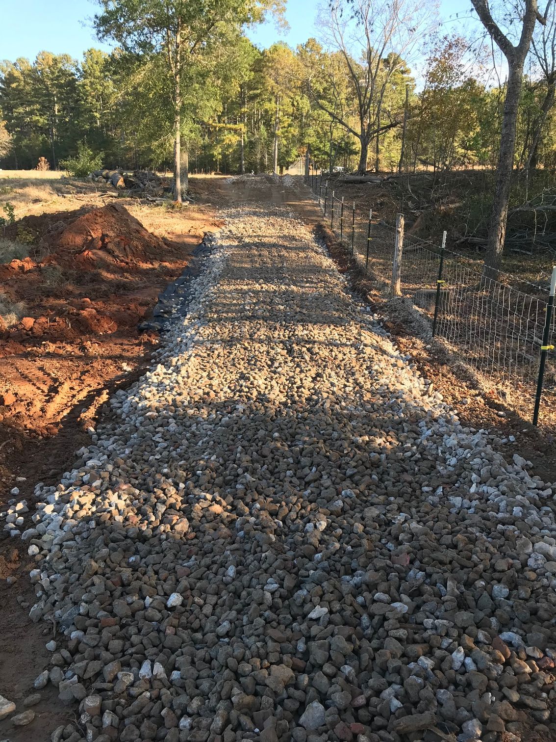 Gravel pathway under construction in a field, surrounded by trees and dirt.