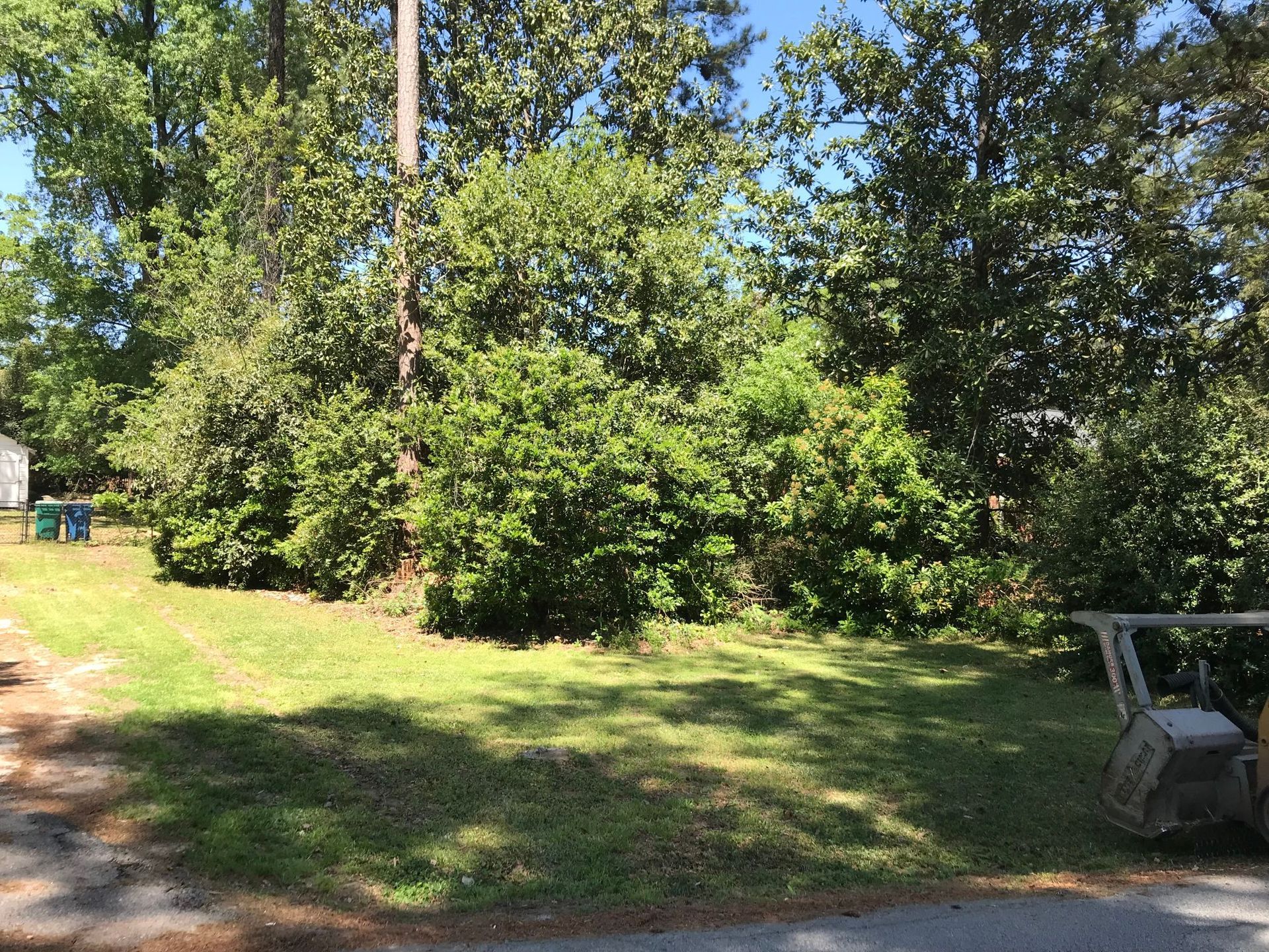 Green grassy yard with dense bushes and trees. A small construction vehicle sits in the corner.