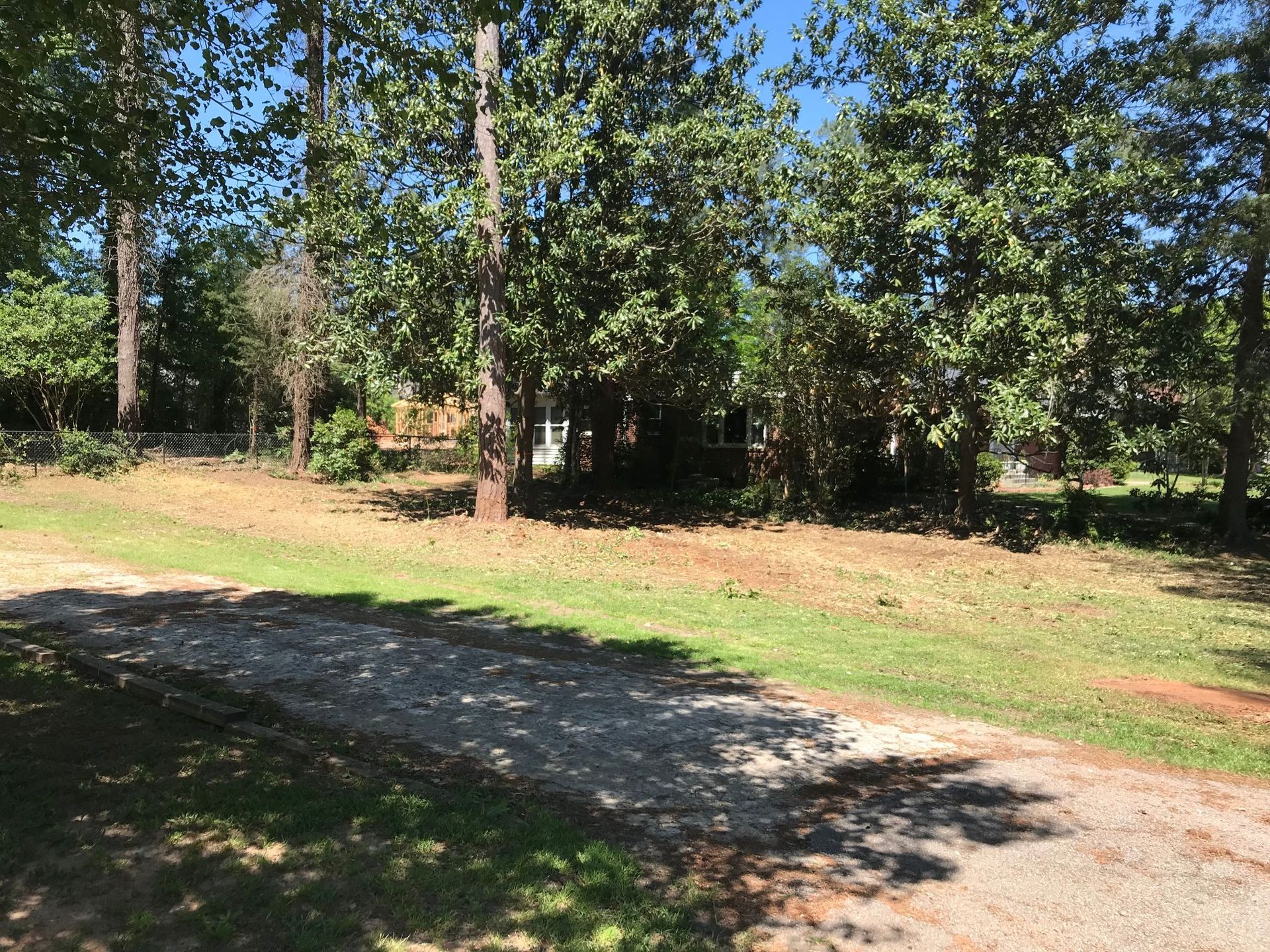 Gravel driveway leading toward trees and a glimpse of a house on a sunny day.