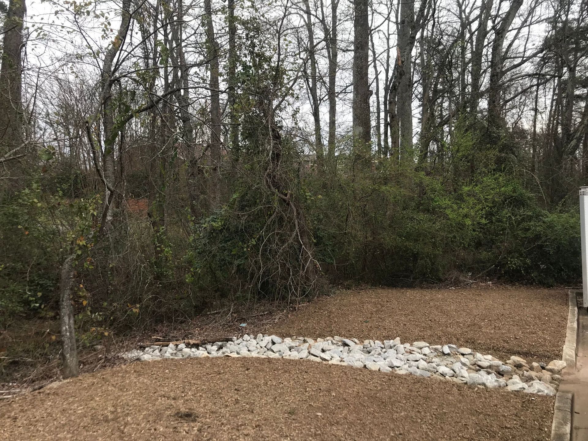 A gravel-filled garden bed with a rock stream and trees in the background.