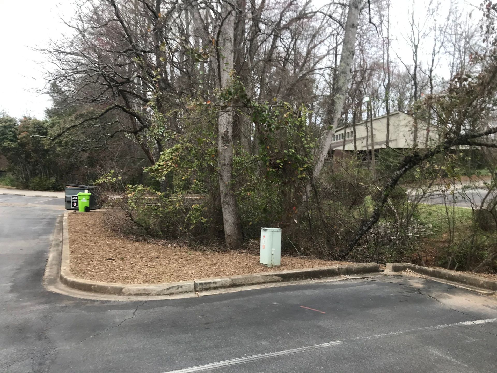 Parking lot with mulch bed, trees, trash cans, and a building in the background.