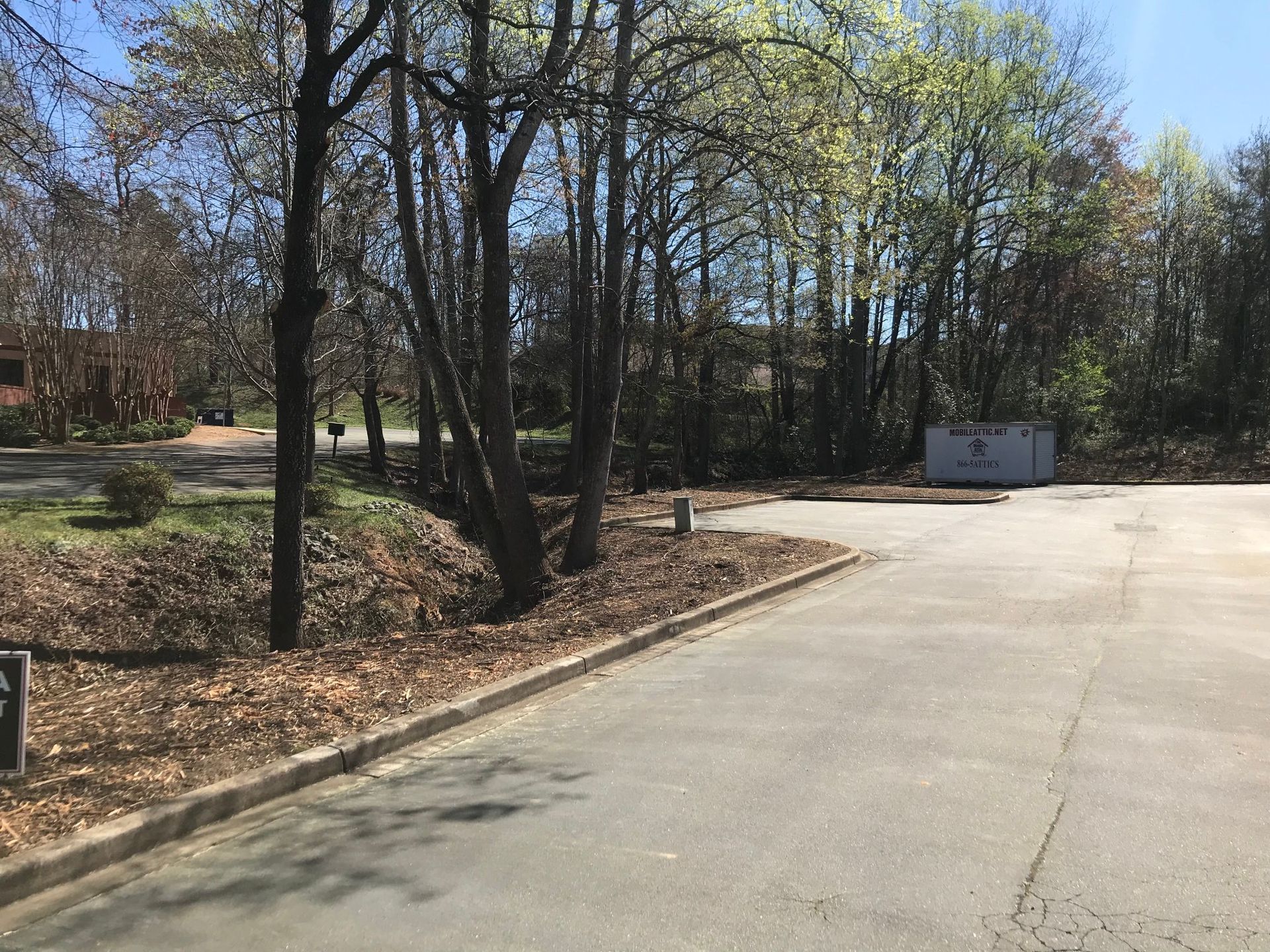 Paved area bordered by trees with fall foliage, leading to a grassy area and a container in the distance.