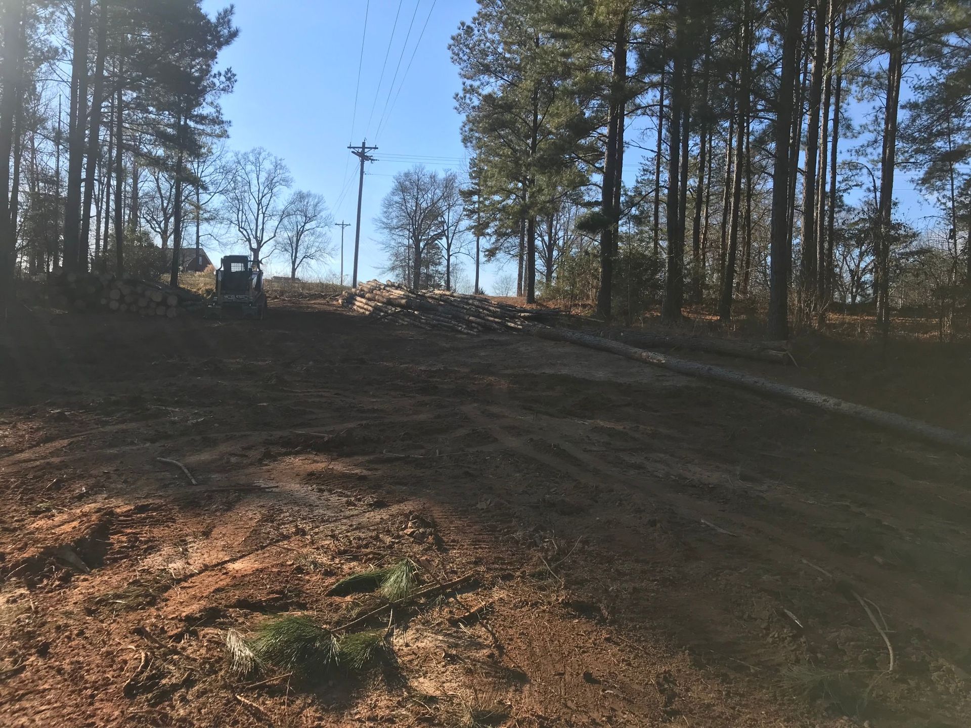 Dirt clearing in a wooded area with a small tractor and trees. Brown dirt and blue sky.