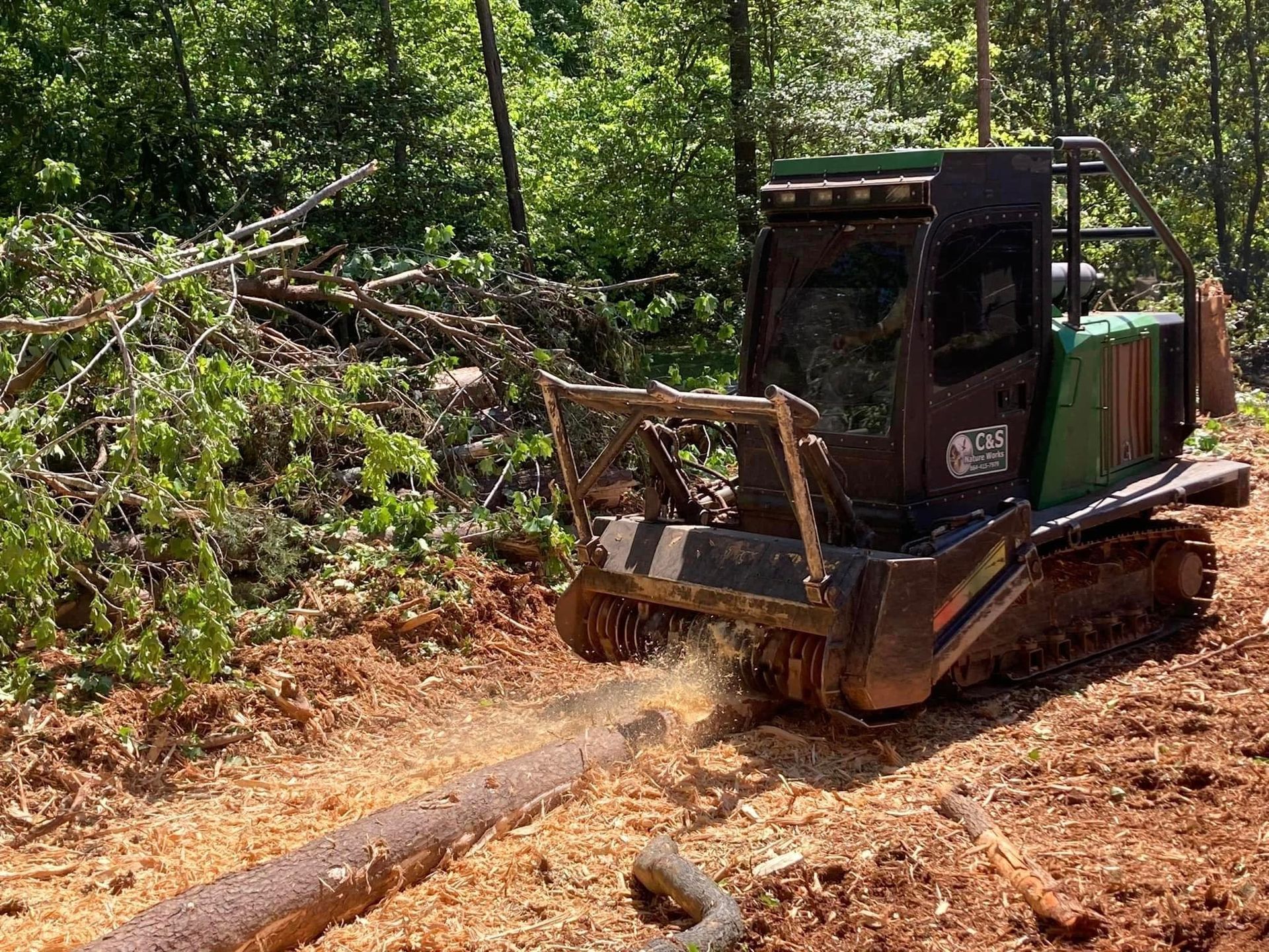 A green and black forestry mulcher grinding a log in a forest, creating wood chips.