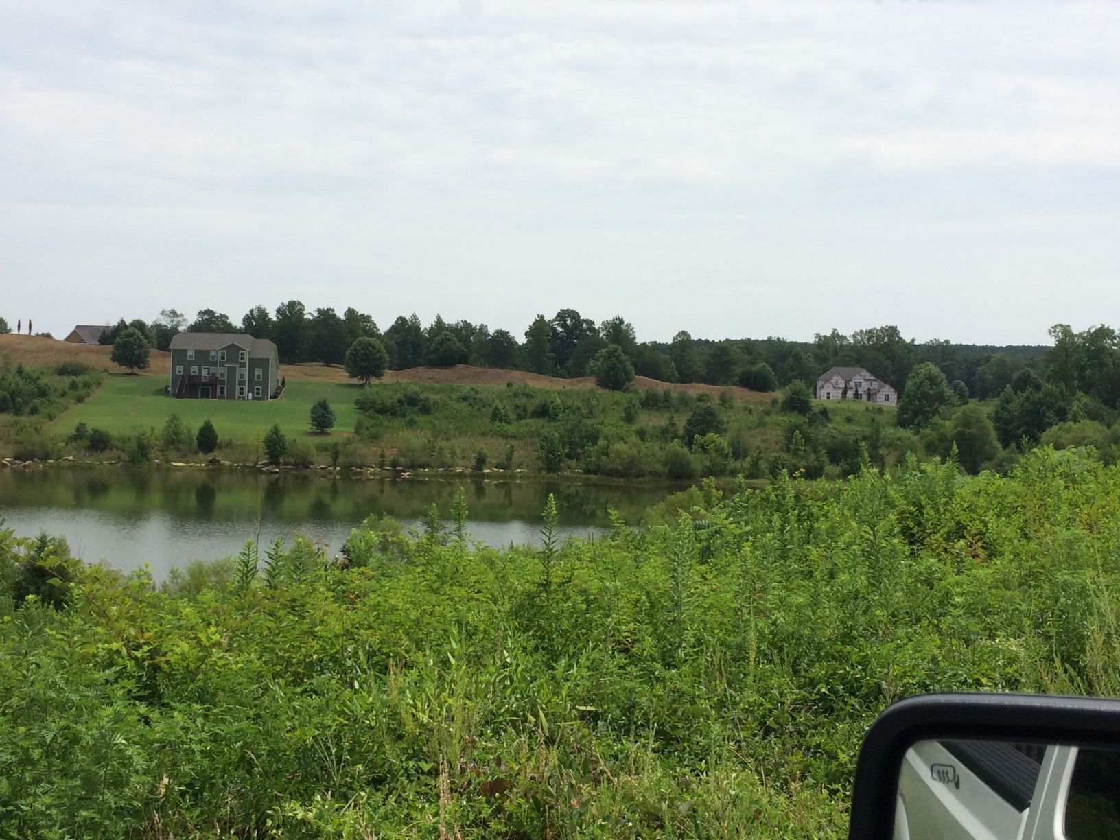 Lakeside homes on a hillside, green vegetation, water, and cloudy sky.