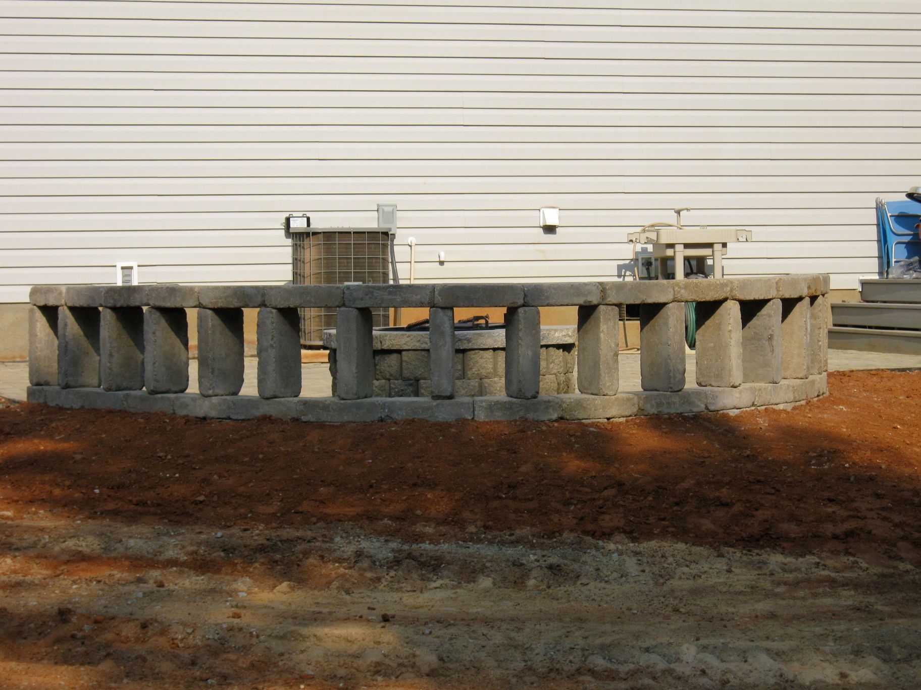 A circular concrete block structure in front of a white wall.