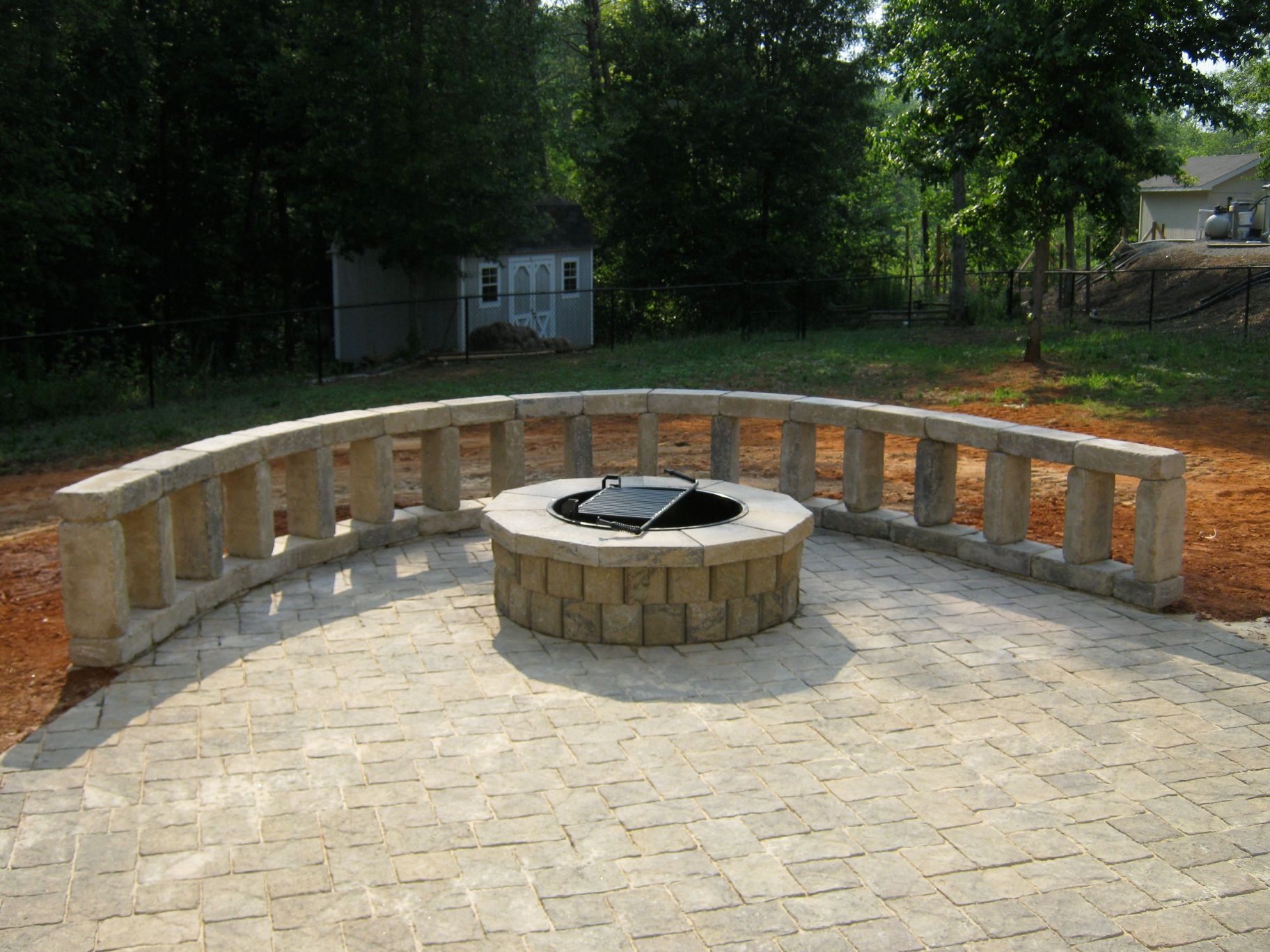Fire pit with curved stone seating on a paved patio, backyard setting.