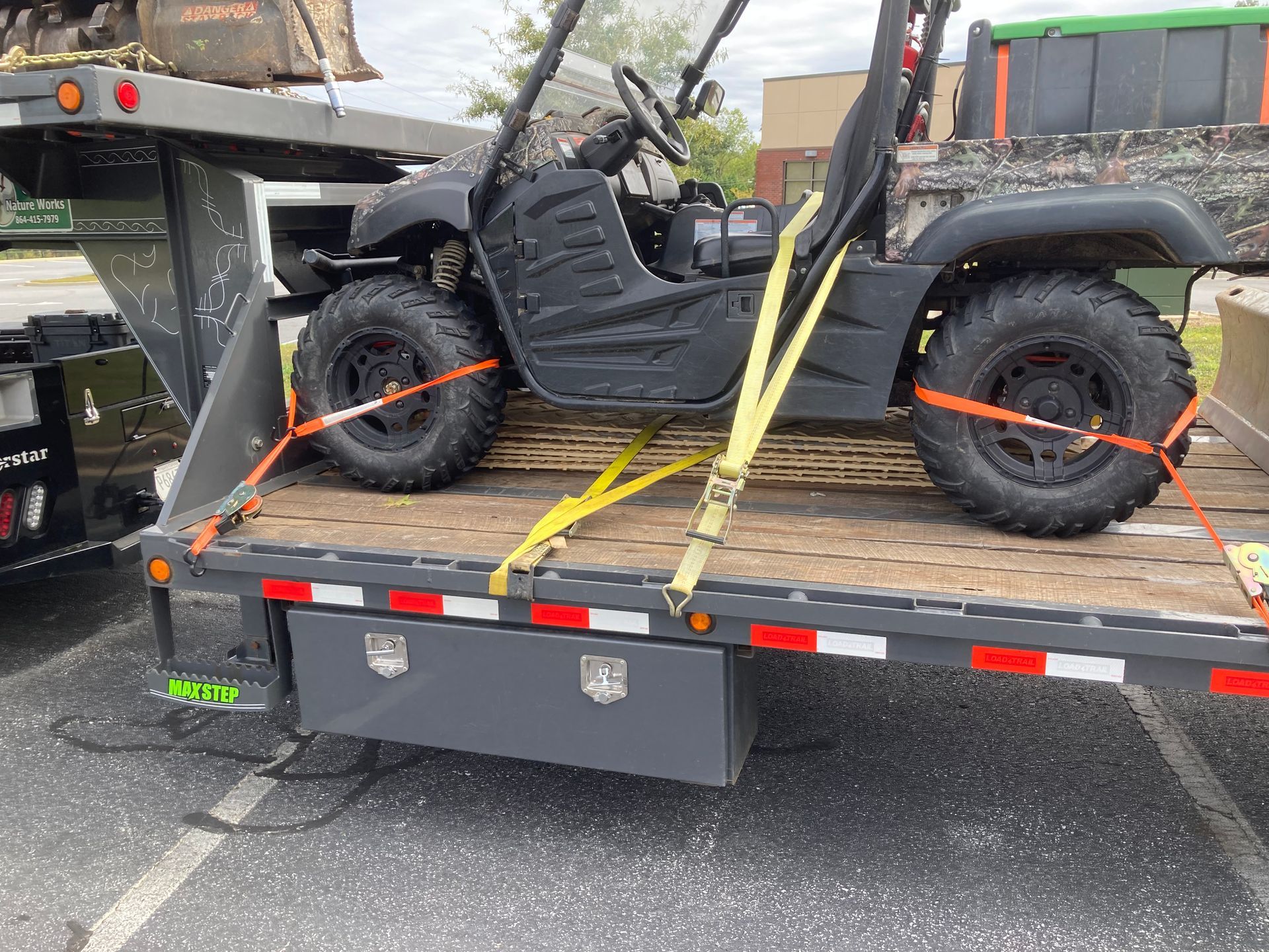 Black golf cart secured with straps on a flatbed trailer. Outdoors, daytime.