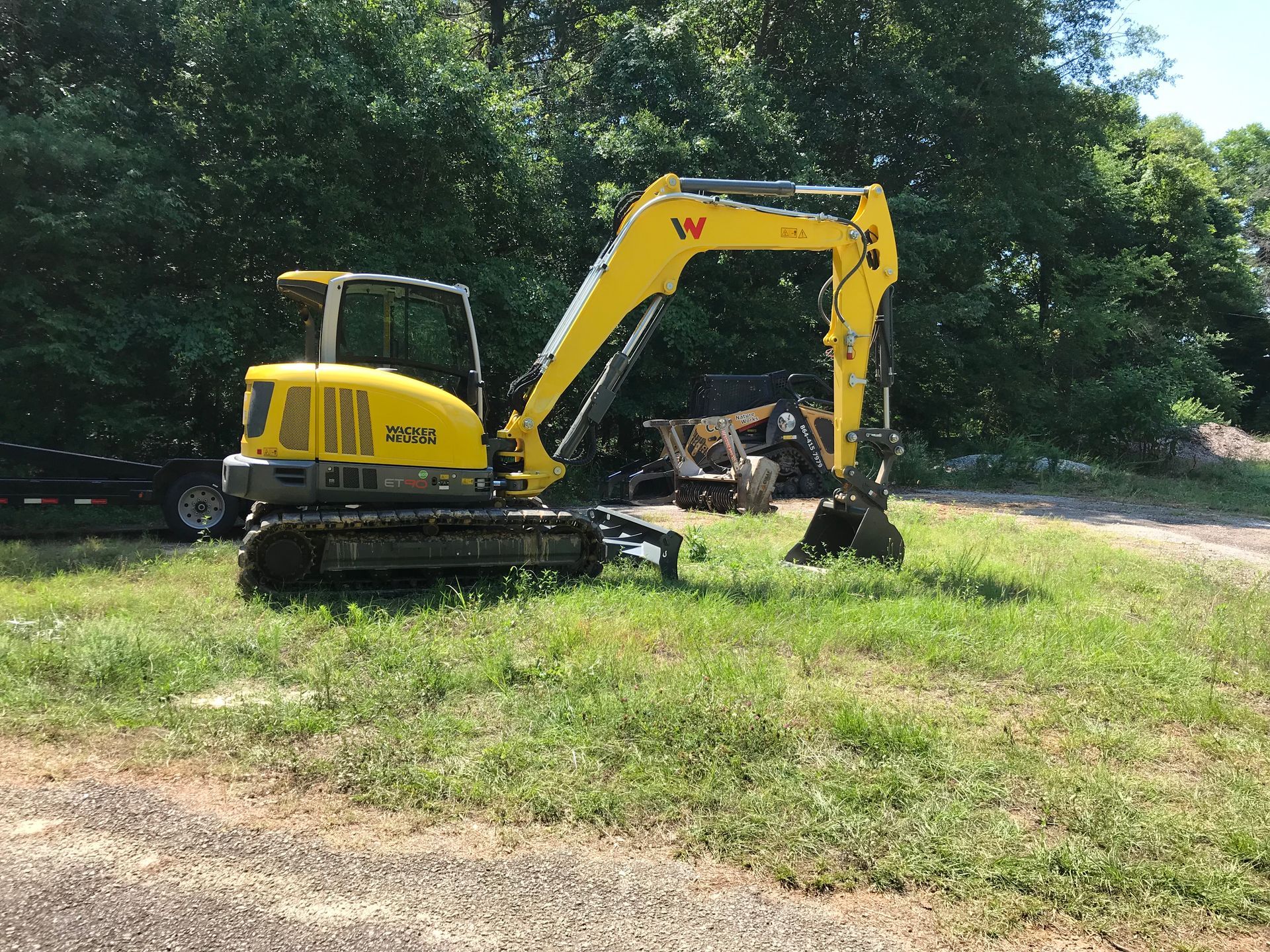 Yellow excavator on grass near trees.