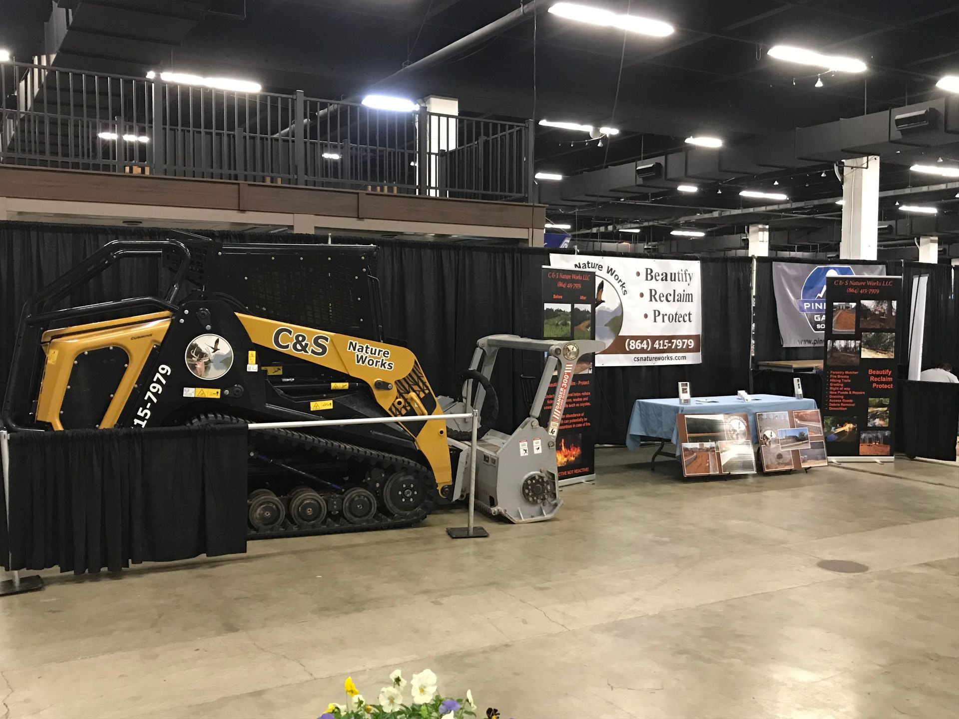 Yellow and black skid steer on display at a trade show booth with product information.