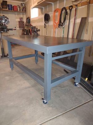 A grey steel workbench on casters sitting in a garage with tools hanging on the back wall.
