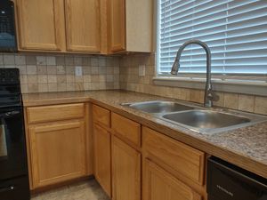 A kitchen corner with oak cabinets, speckled laminate countertops, a stainless steel double sink, and a tiled backsplash.