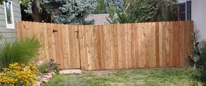 A wooden fence with a gate, installed in a yard with a garden and lawn.