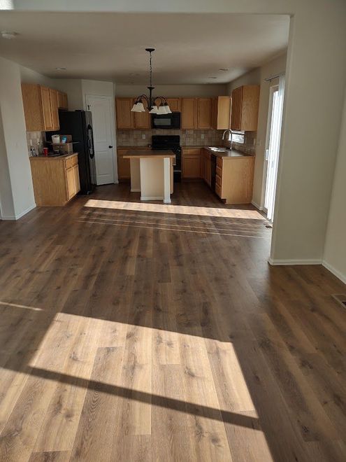 A bright, open-plan kitchen featuring light wood cabinets, brown wood-look flooring, and a central kitchen island.