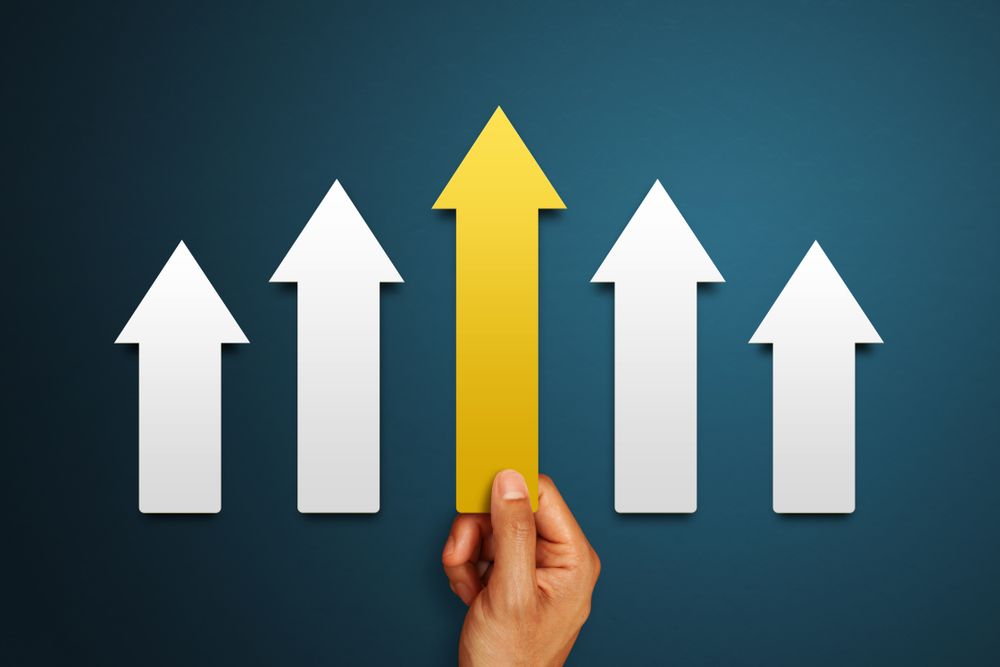 Hand holding a gold arrow pointing upward among white arrows on a dark blue background.