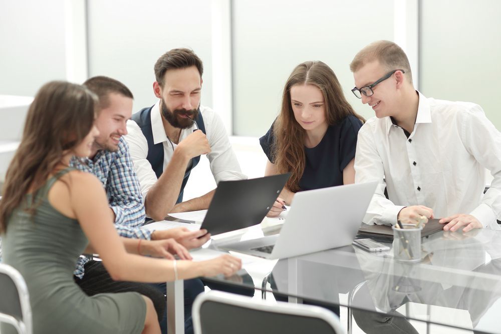 Team of five colleagues collaborating around a table with papers and laptops in a bright office.