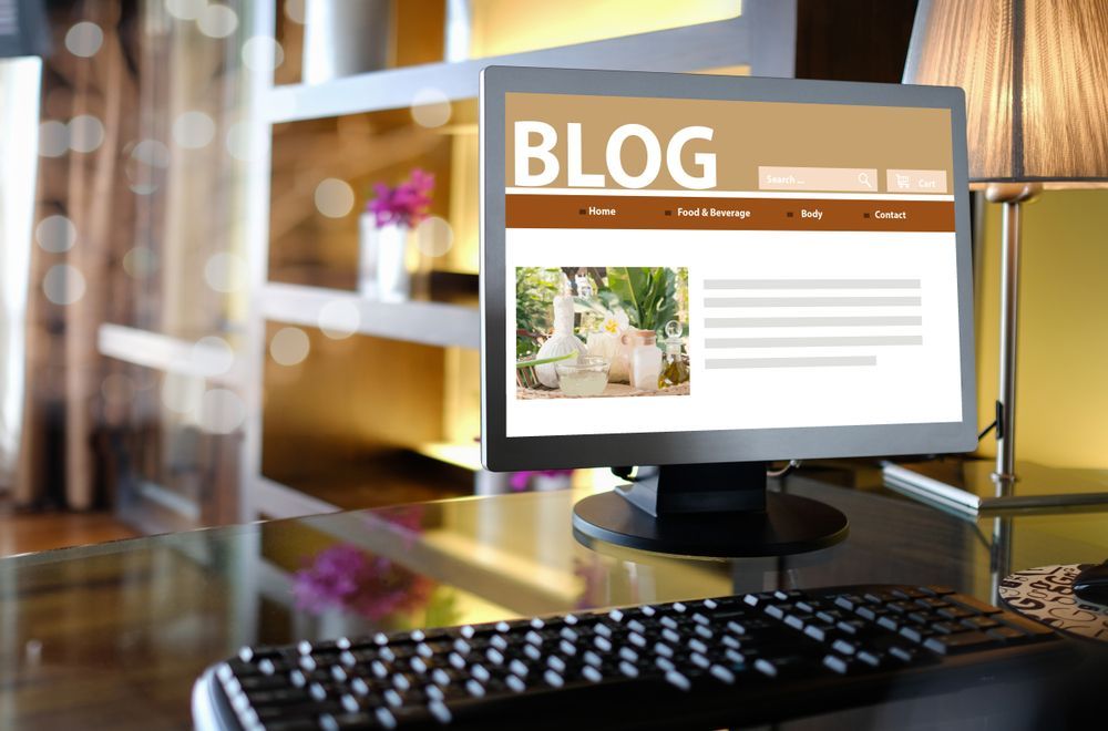 Computer monitor displaying a blog webpage with a photo, next to a keyboard and lamp.