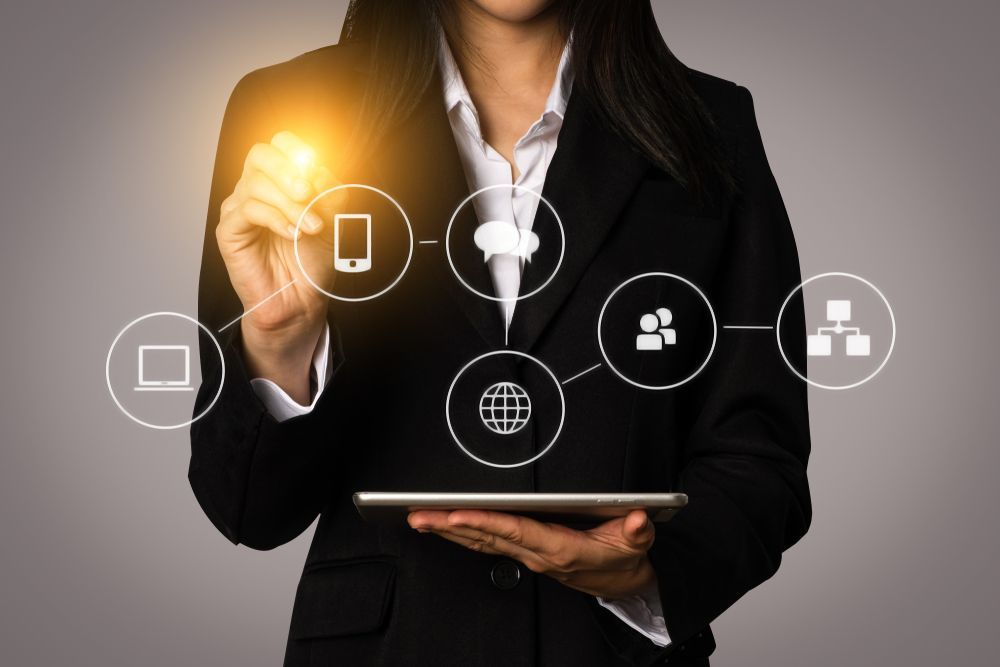 Woman in suit holding tablet, pointing to digital icons.