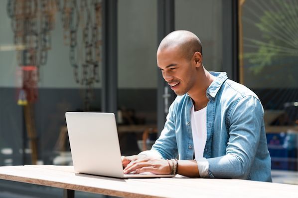 A man is sitting at a table using a laptop computer.