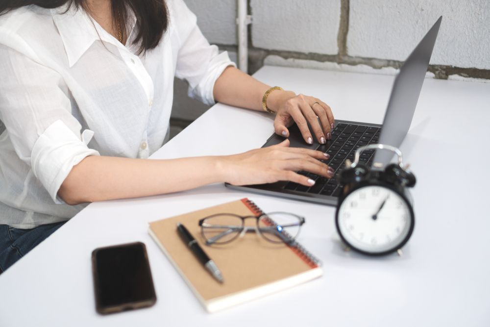 A woman is sitting at a desk typing on a laptop computer.