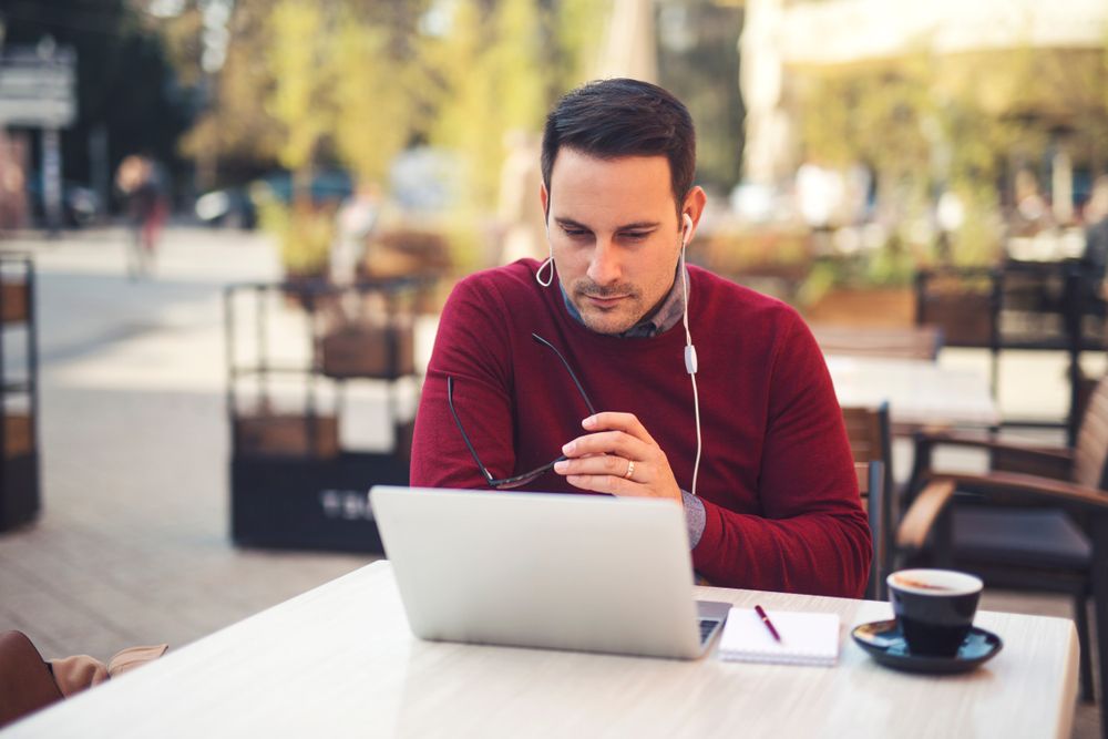 A man is sitting at a table watching a video on a laptop computer.