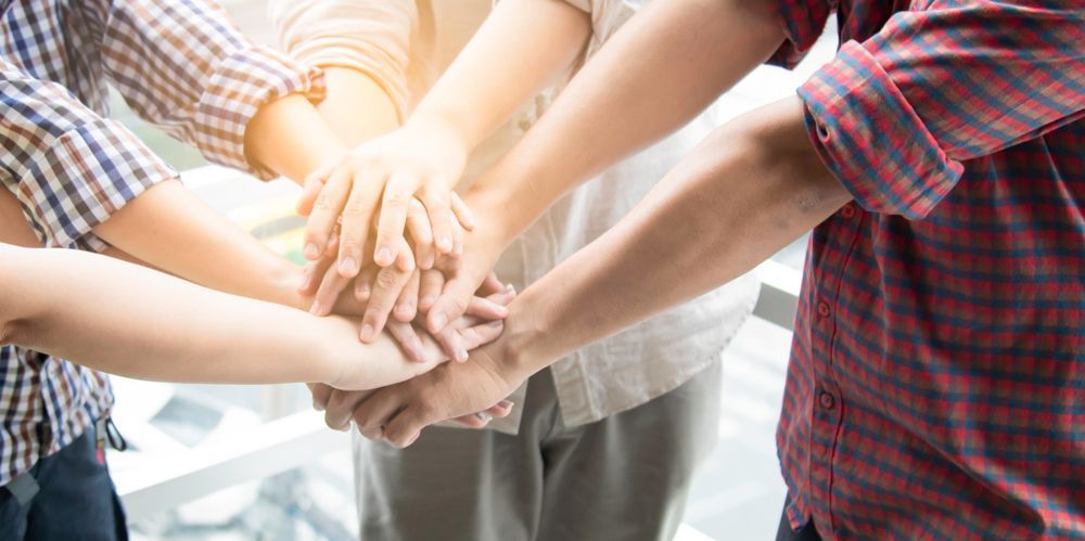 Group of people with hands stacked on top of each other in a team huddle.