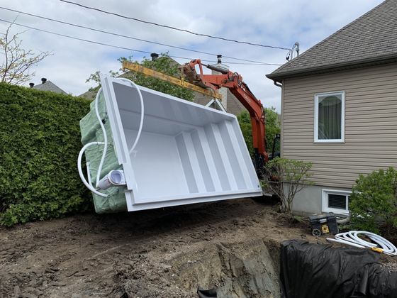 Une grande piscine blanche est en cours d'installation devant une maison.