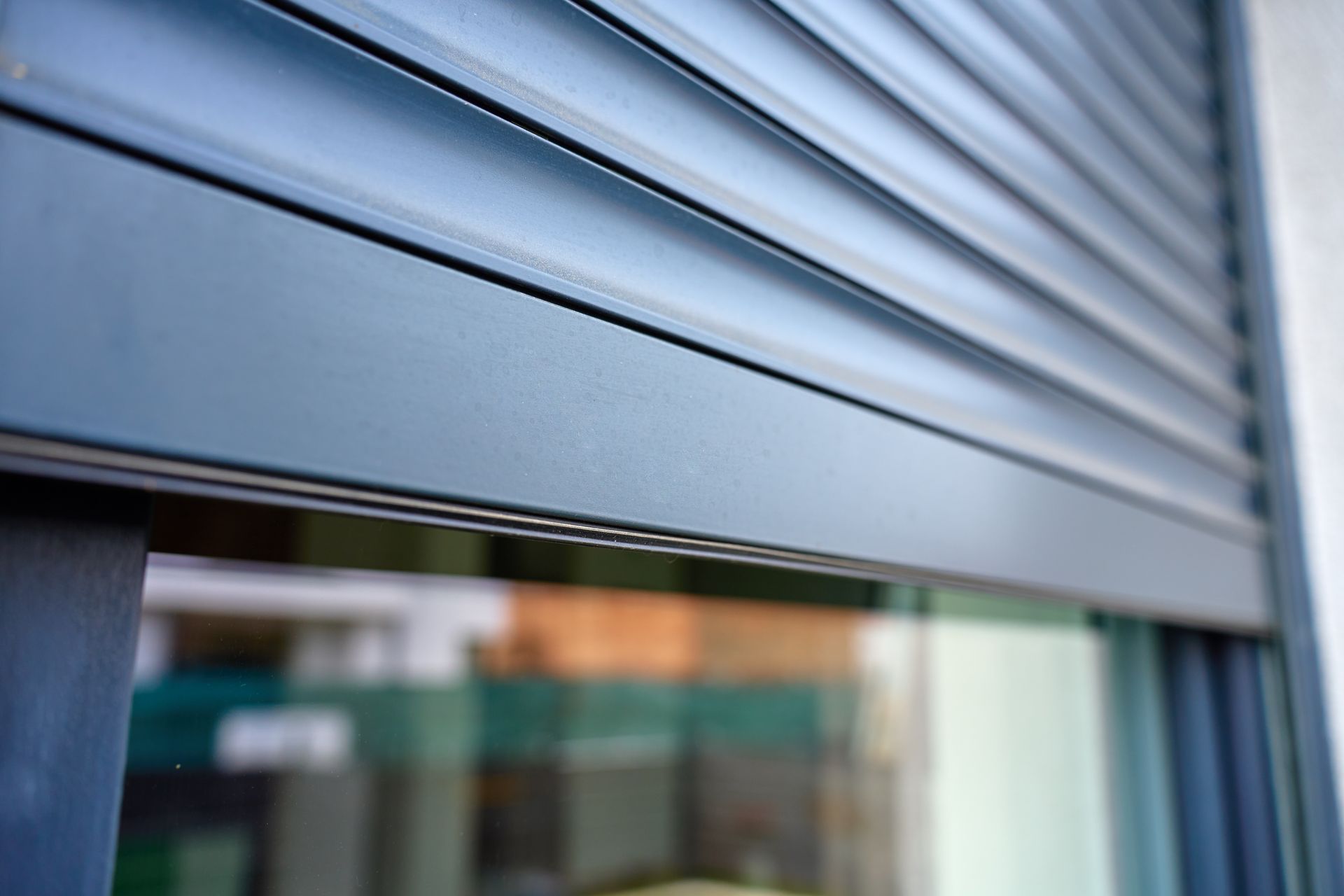 A close-up of a modern metal roller shutter partially covering a window on a building exterior.