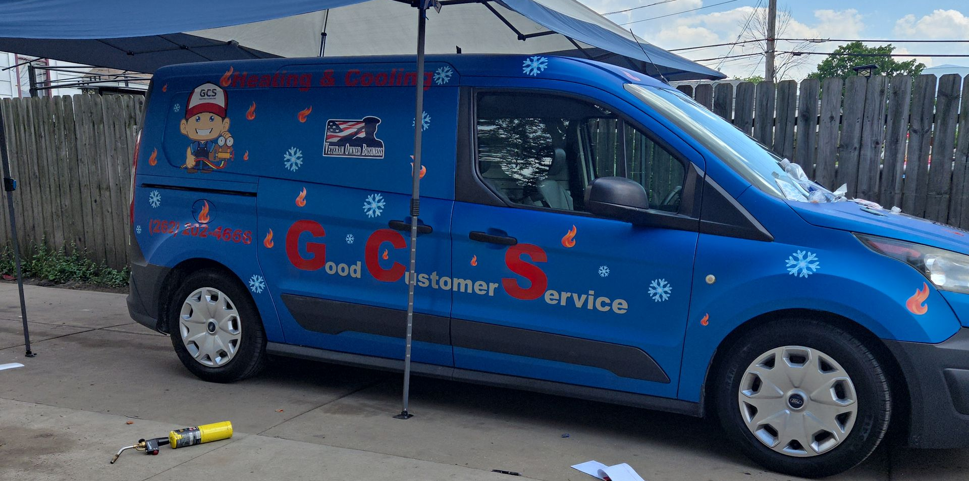 Person attaching gauges to an air conditioning unit, with blue and red hoses and gauges. HVAC GCS van