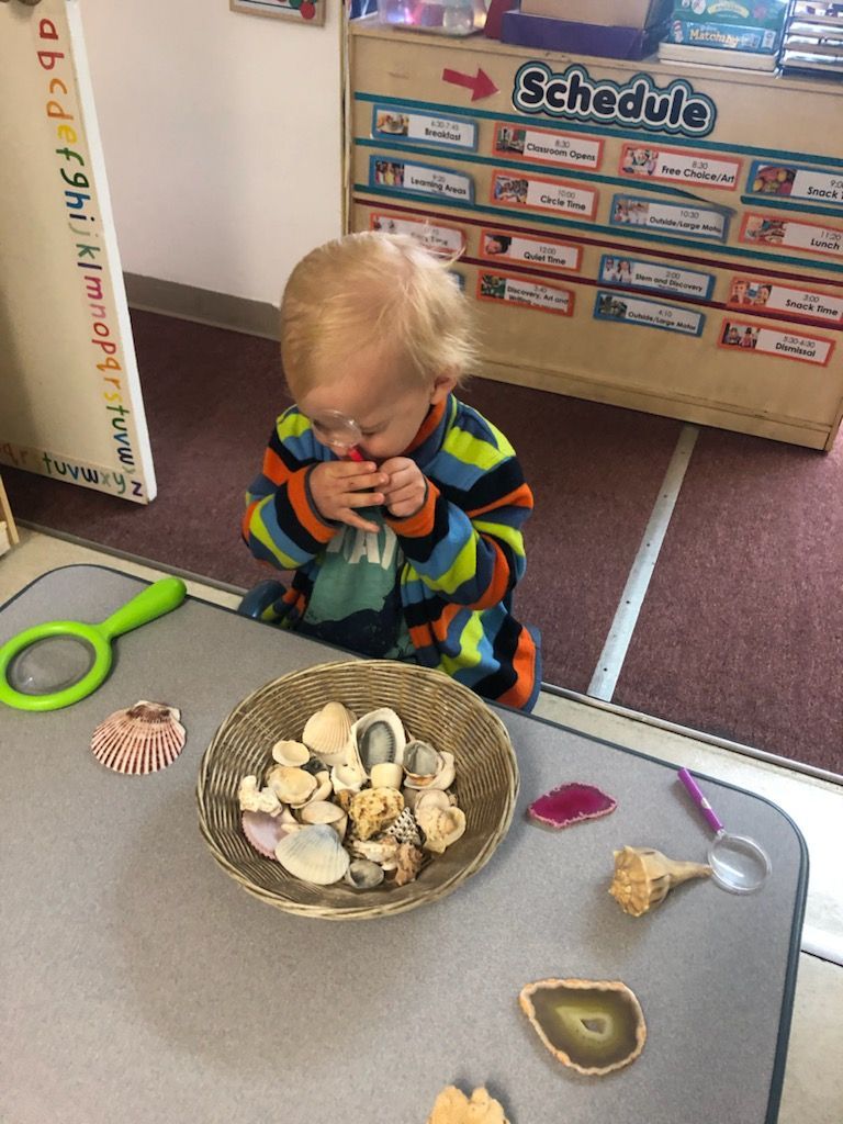 Young child in lab coat and goggles pouring liquid into a beaker, surrounded by colorful beakers.