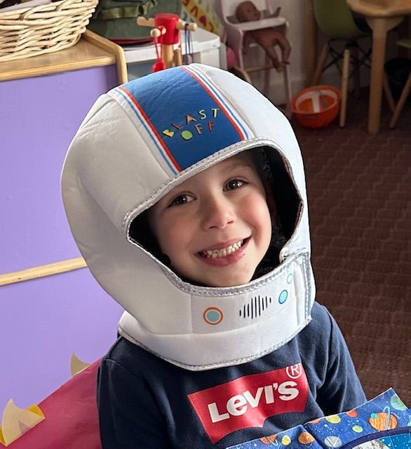 Child wearing a yellow helmet, riding a red tricycle outdoors.