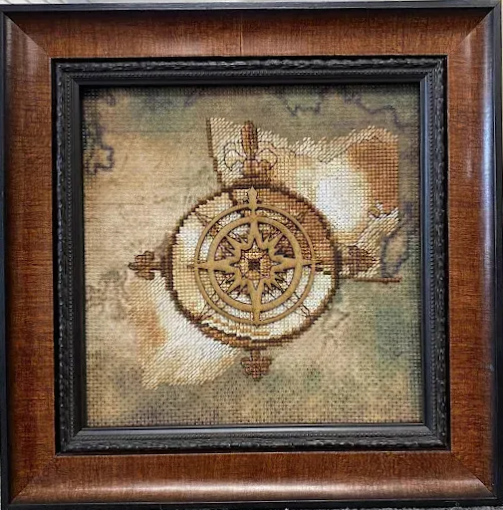 Cross-stitch compass and map artwork framed in dark wood.