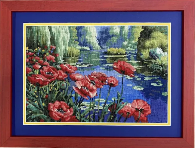 Framed cross-stitch art depicting red poppies and water lilies in a blue pond, with weeping willow trees.