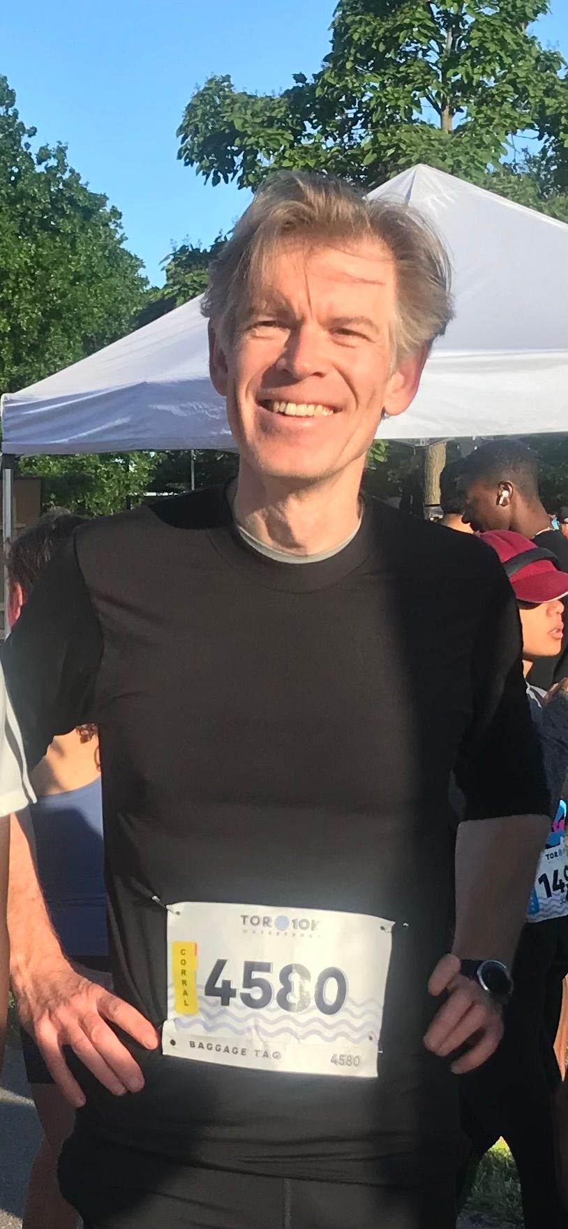 Man wearing bib number 4580, smiling, standing outside near a white tent.