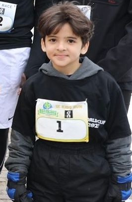 Boy wearing bib with number 1, standing outdoors, wearing black long-sleeve shirt.