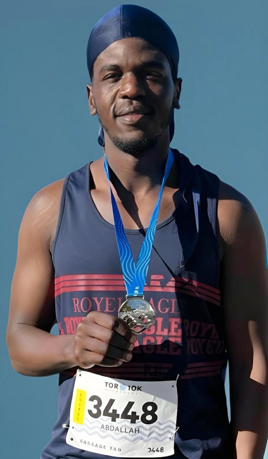 Athlete in blue tank top and durag holds a medal. Race bib 3448 visible.