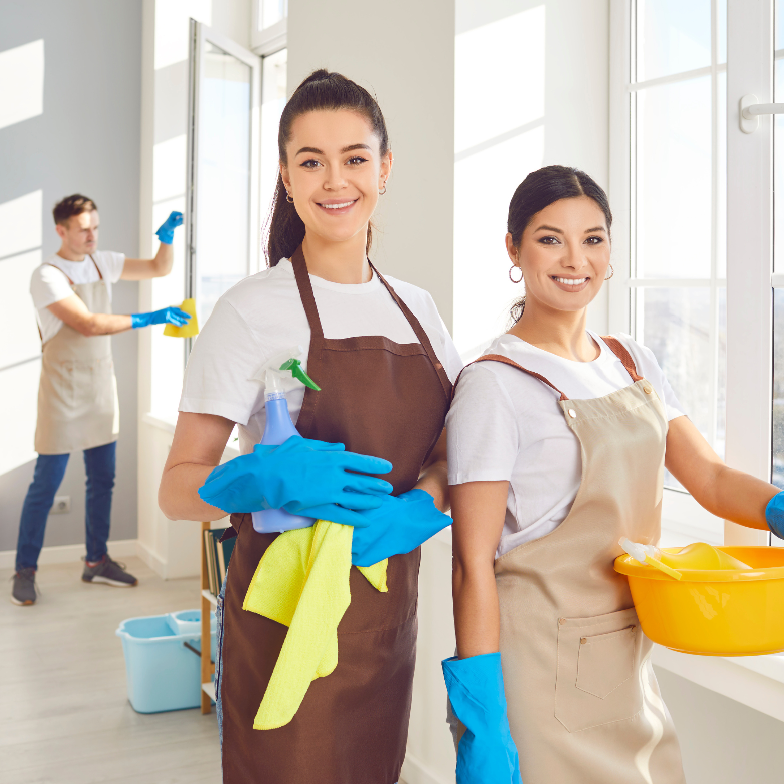 Two women are standing next to each other in a room holding cleaning supplies.