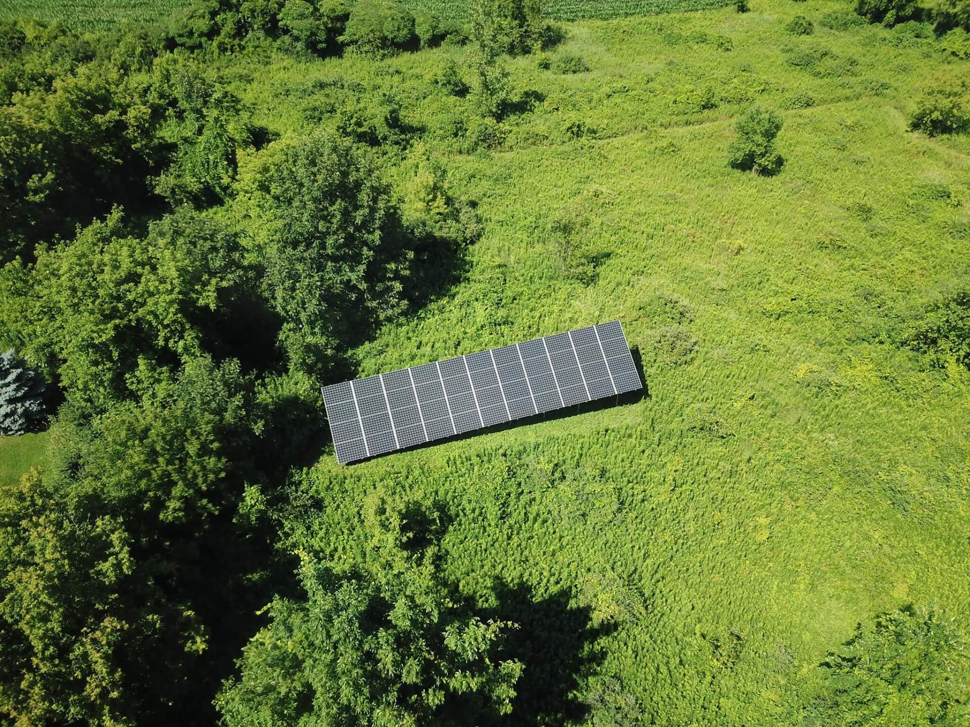 an aerial view of a solar panel in a field surrounded by trees 