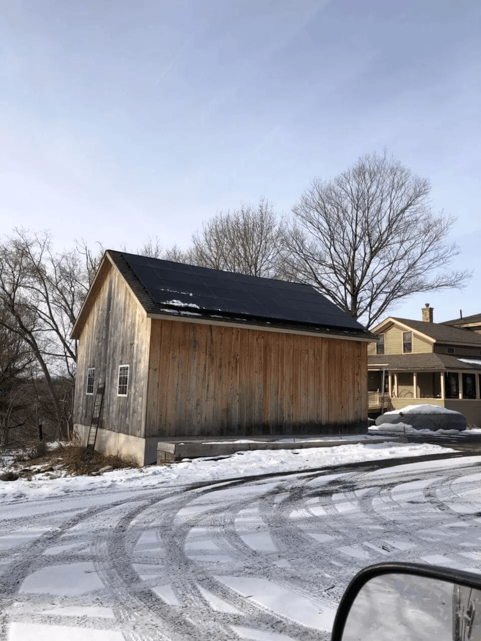 a wooden barn with solar panels on the roof is sitting in the snow .