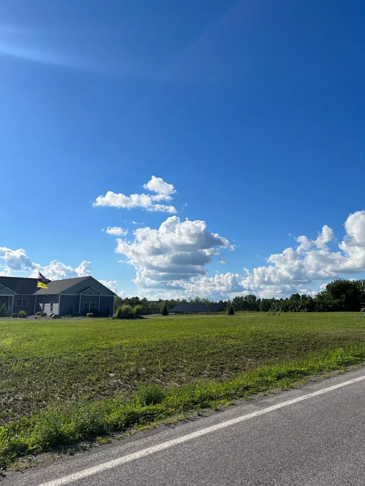 a house is sitting in the middle of a grassy field next to a road 
