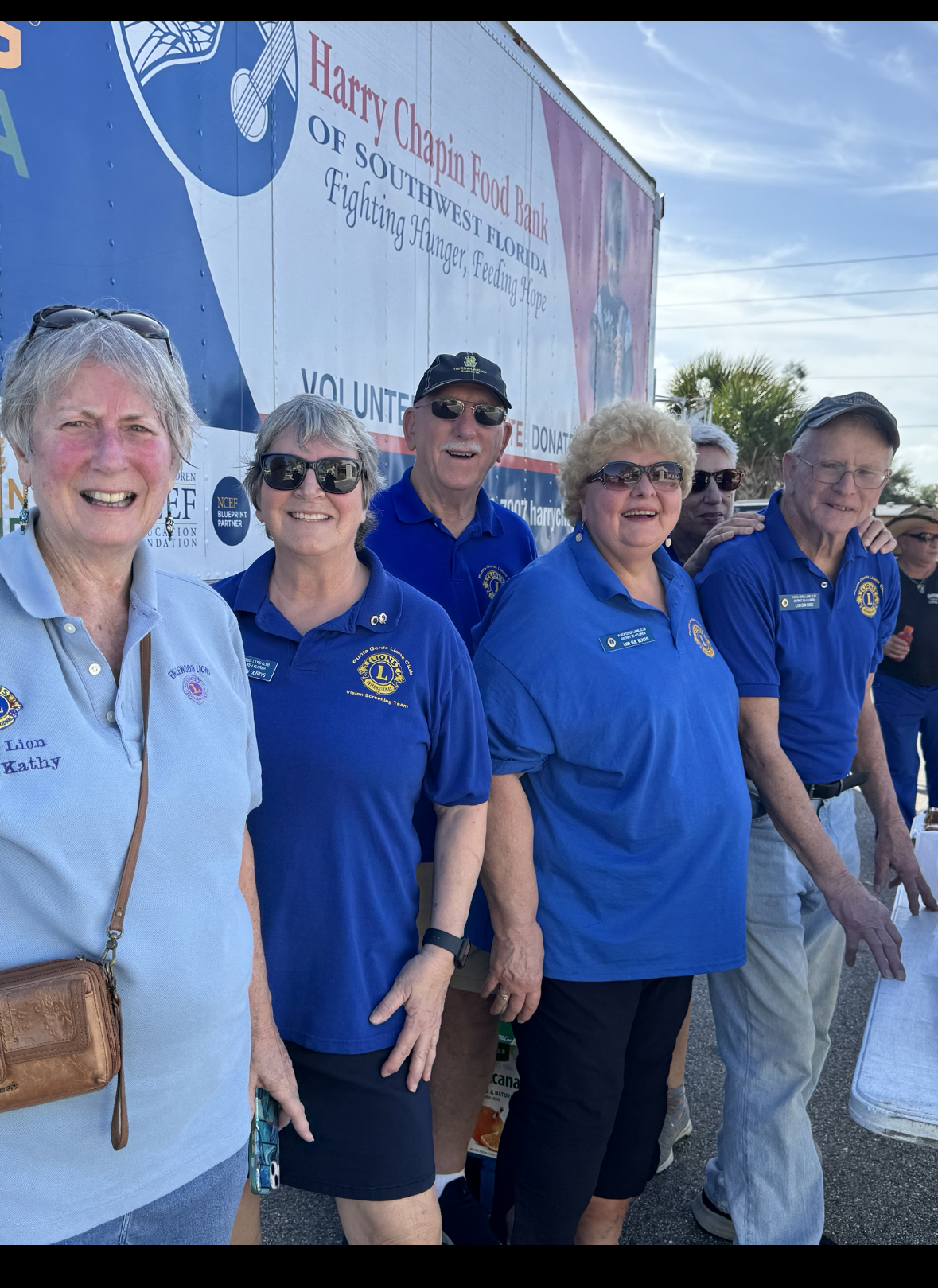 Group of Lions Club members wearing blue shirts, smiling outside a trailer.