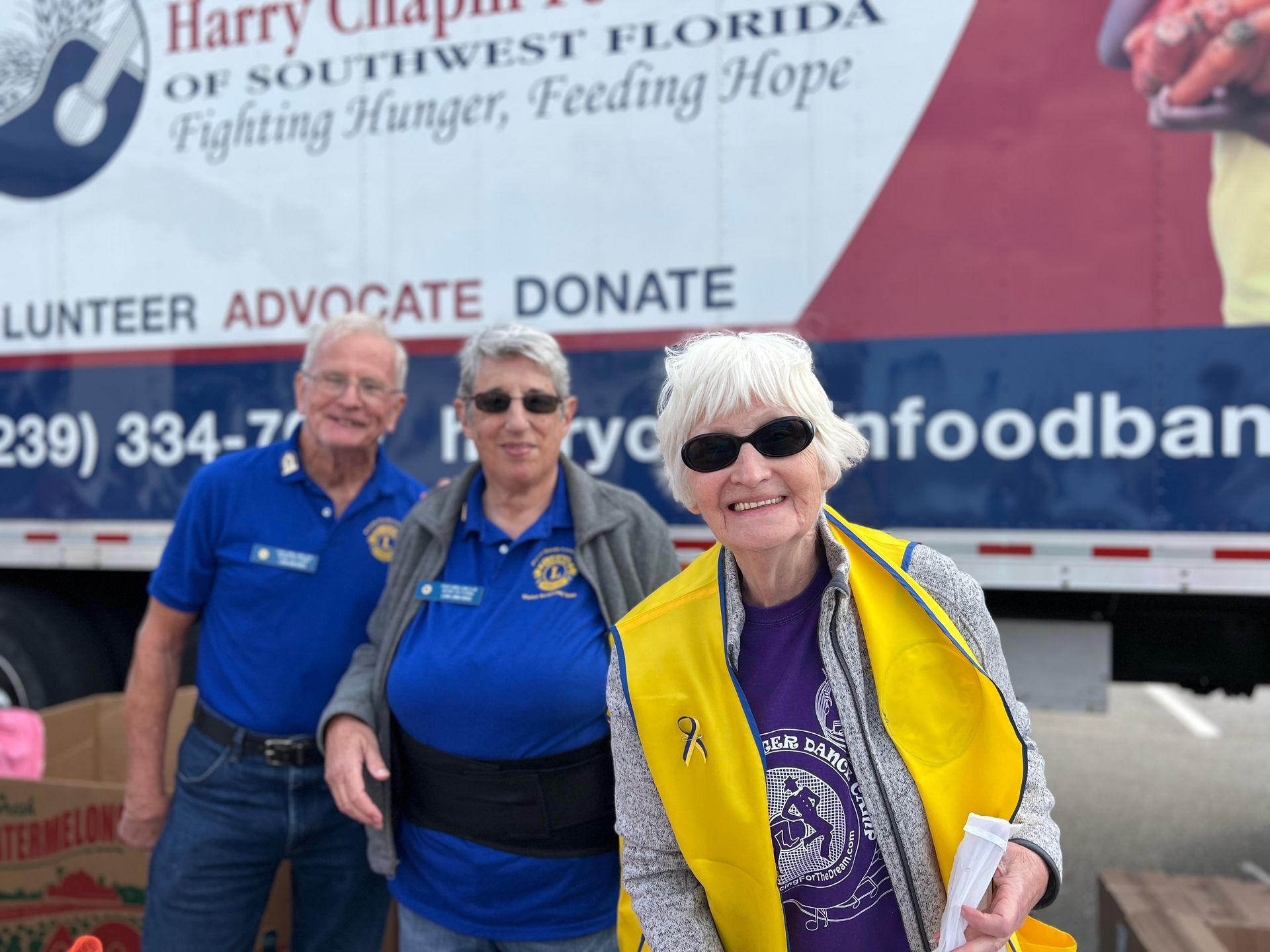Three volunteers smile in front of a food bank truck with text.