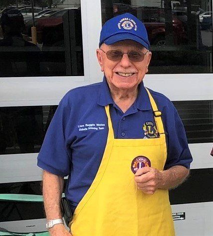 Smiling elderly man in blue shirt and cap, yellow apron, Lions Club logo.
