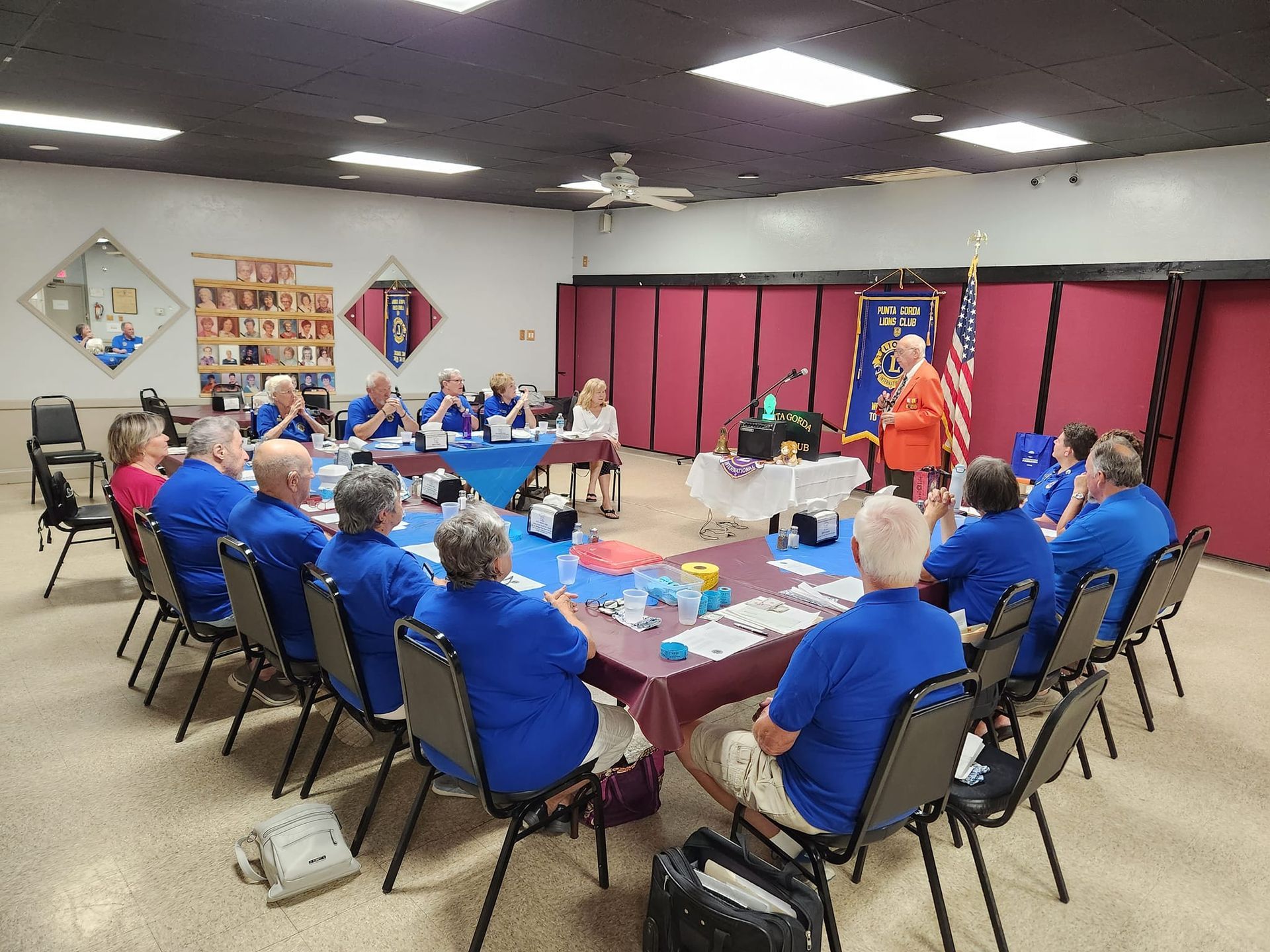 Group of people in blue shirts at a meeting, gathered around a table. American flag in the background.