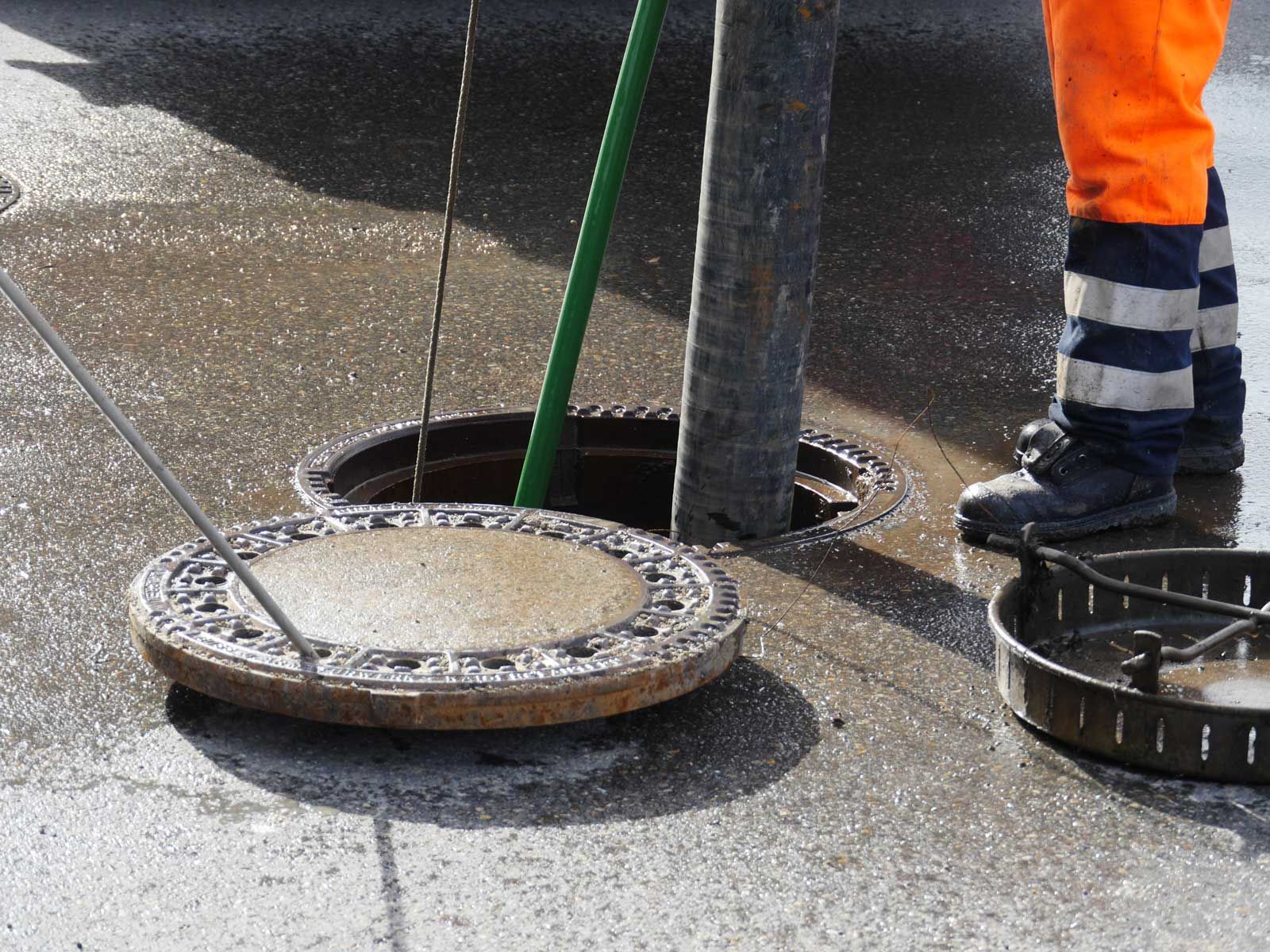 A worker using high pressure equipment to clean a sewer line through an open manhole. A worker using high pressure equipment to clean a sewer line through an open manhole.