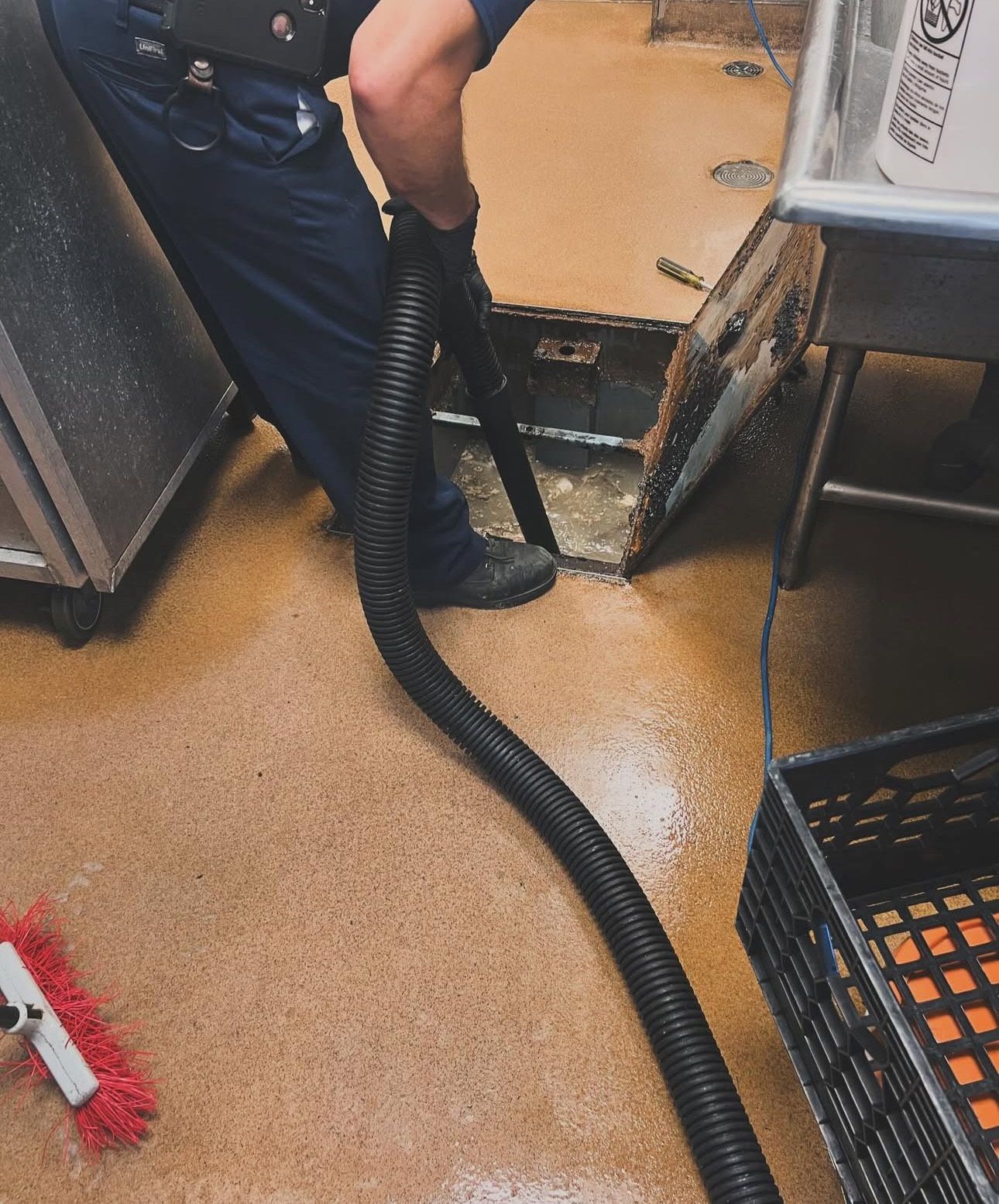 Person using a hose to extract water from a flooded kitchen floor, likely cleaning up.
