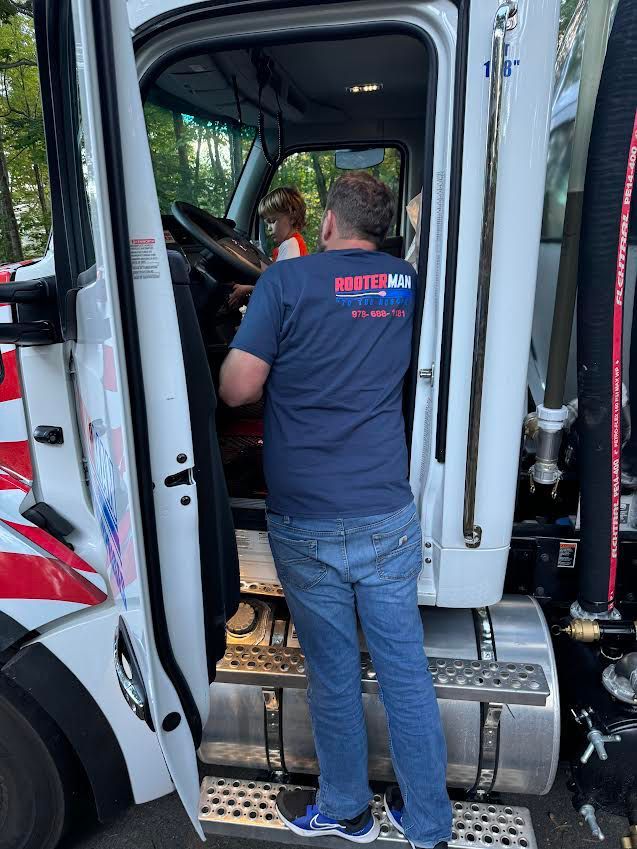 Man in a blue shirt stands in the doorway of a white semi-truck; another person sits inside.