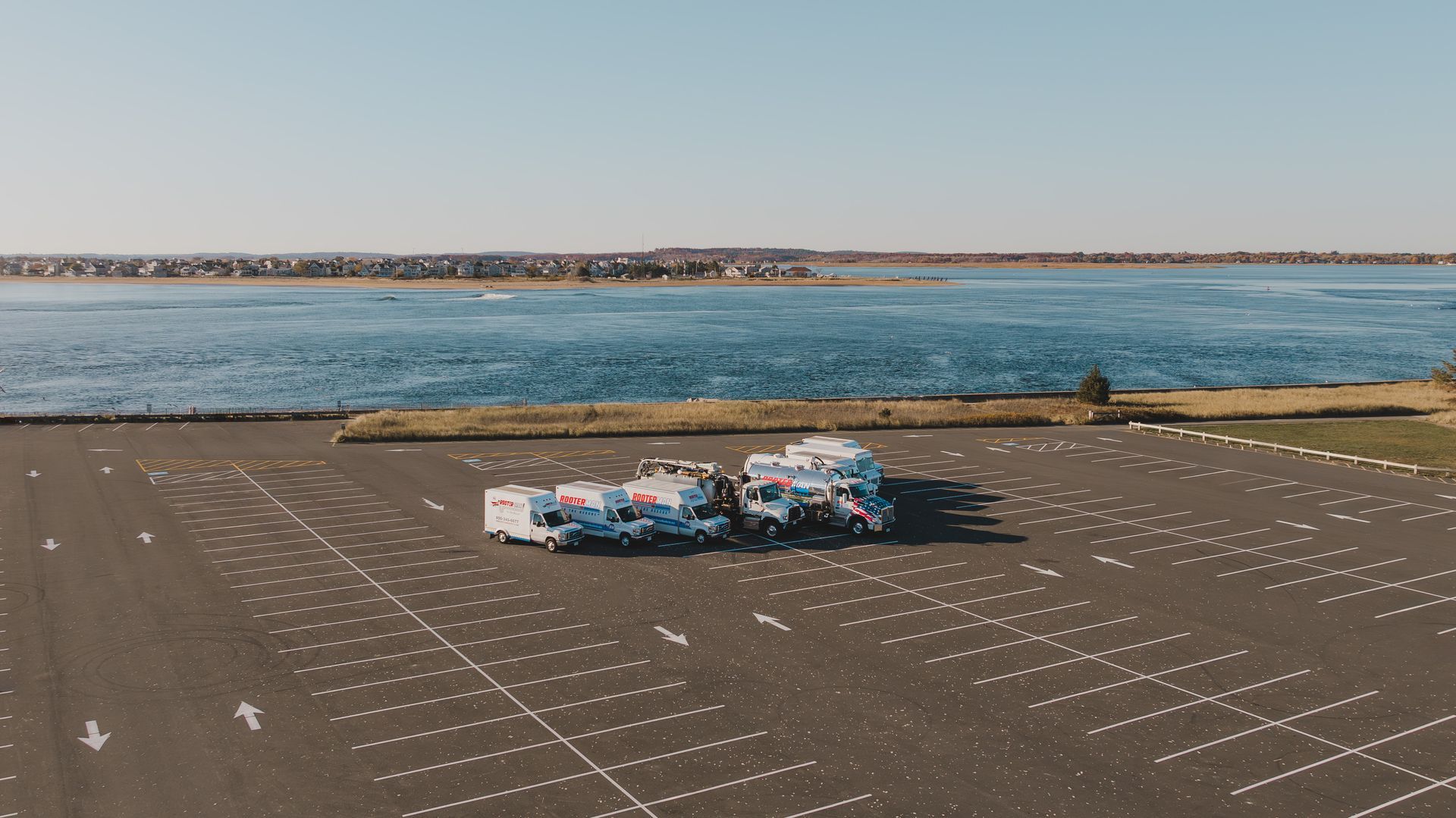 Plumber using an orange wrench to fix a silver sink drain pipe. White tile background.
